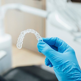 Orthodontist holding clear aligner with blue gloves