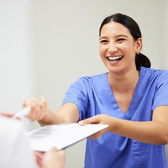 Dental assistant smiling while handing patient form