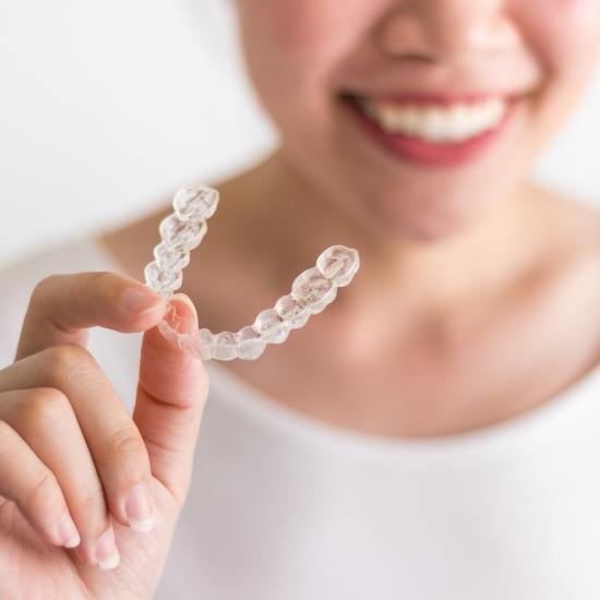 Smiling person holding an Invisalign clear aligner in Wayland