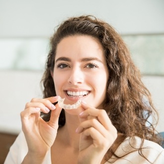Smiling woman placing Invisalign aligner into her mouth
