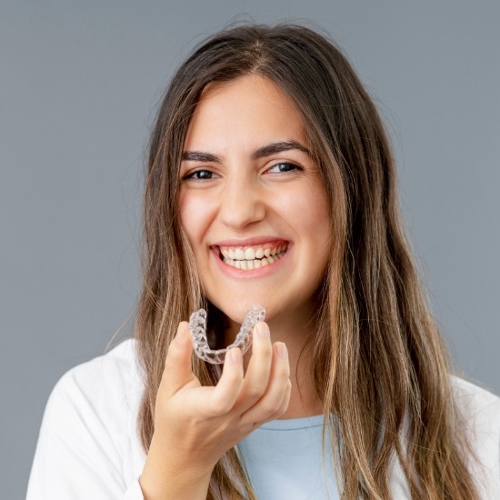 Smiling teen girl holding an Invisalign aligner in Wayland