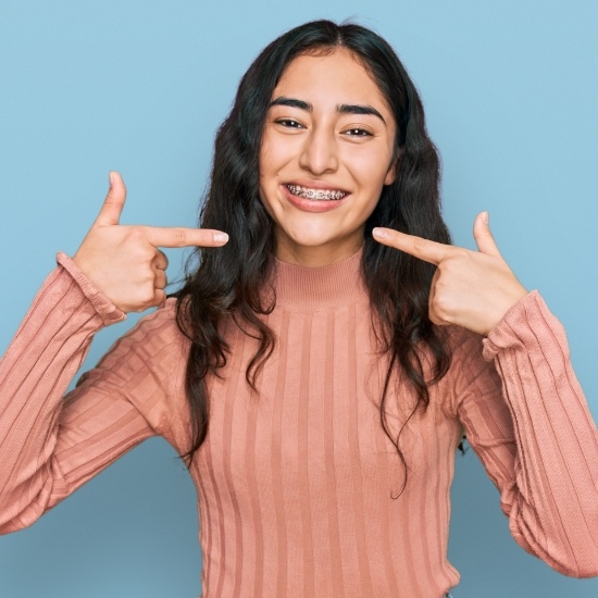 Young woman pointing to her smile with traditional braces in Wayland