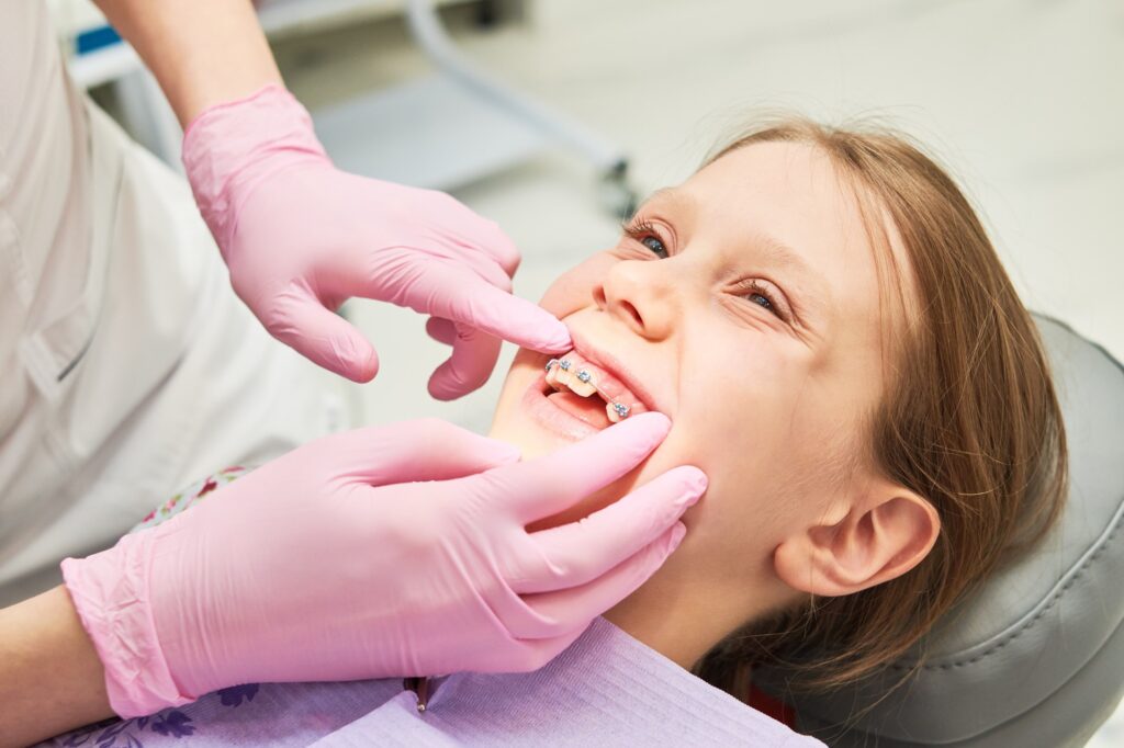 Child with braces smiling while orthodontist examines their teeth