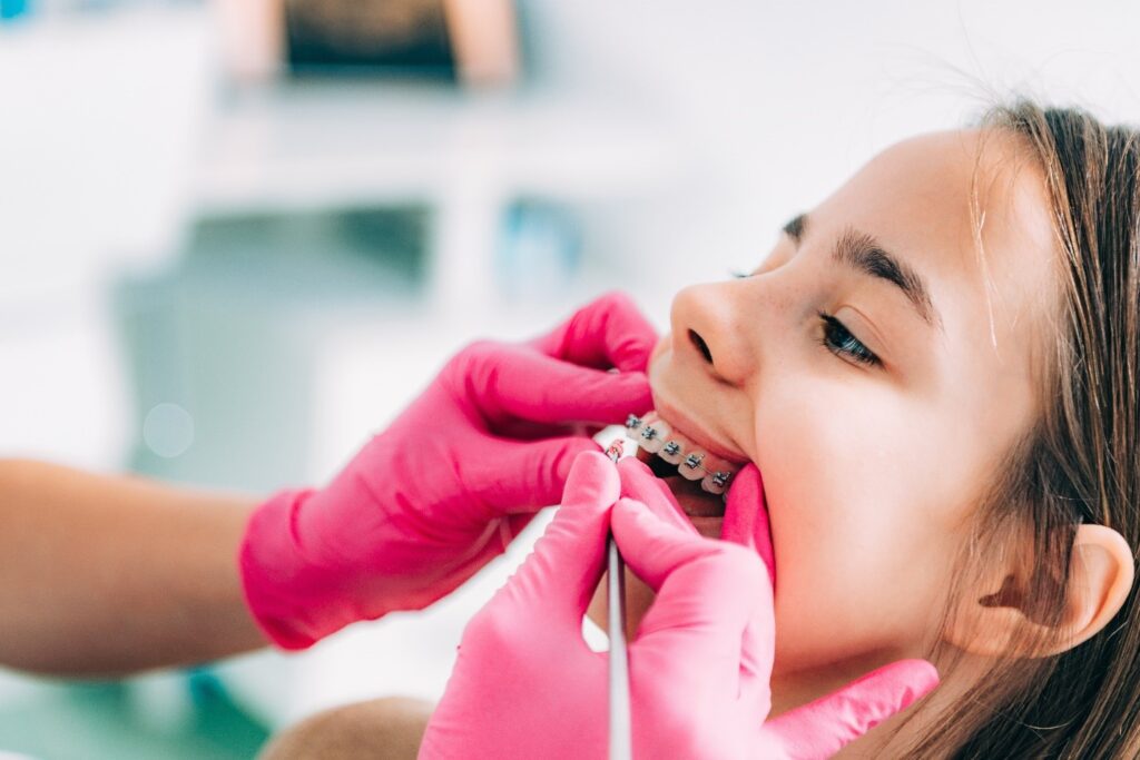 Orthodontist with pink gloves checking patient's braces